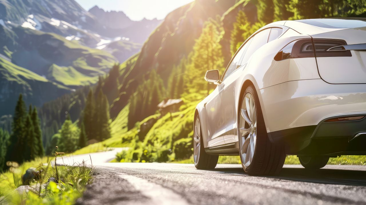 Eine schmale Strasse in den Bergen. Sommerliches Wetter, die Sonne scheint. Ein Elektroauto fährt die Strasse runter.