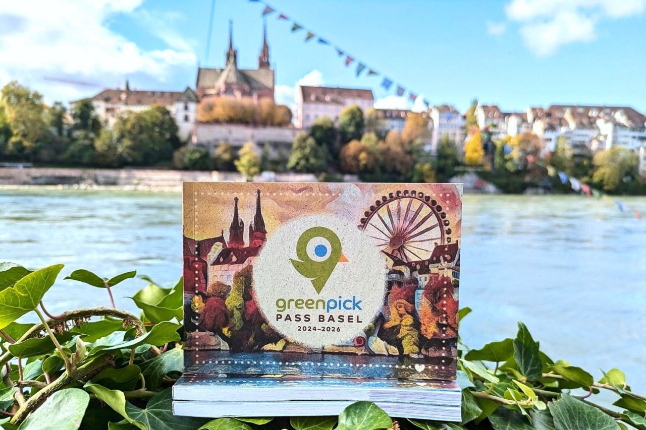 GreenPick Pass steht auf einer Mauer vor dem Rhein, im Hintergrund ist das Basler Münster zu sehen.