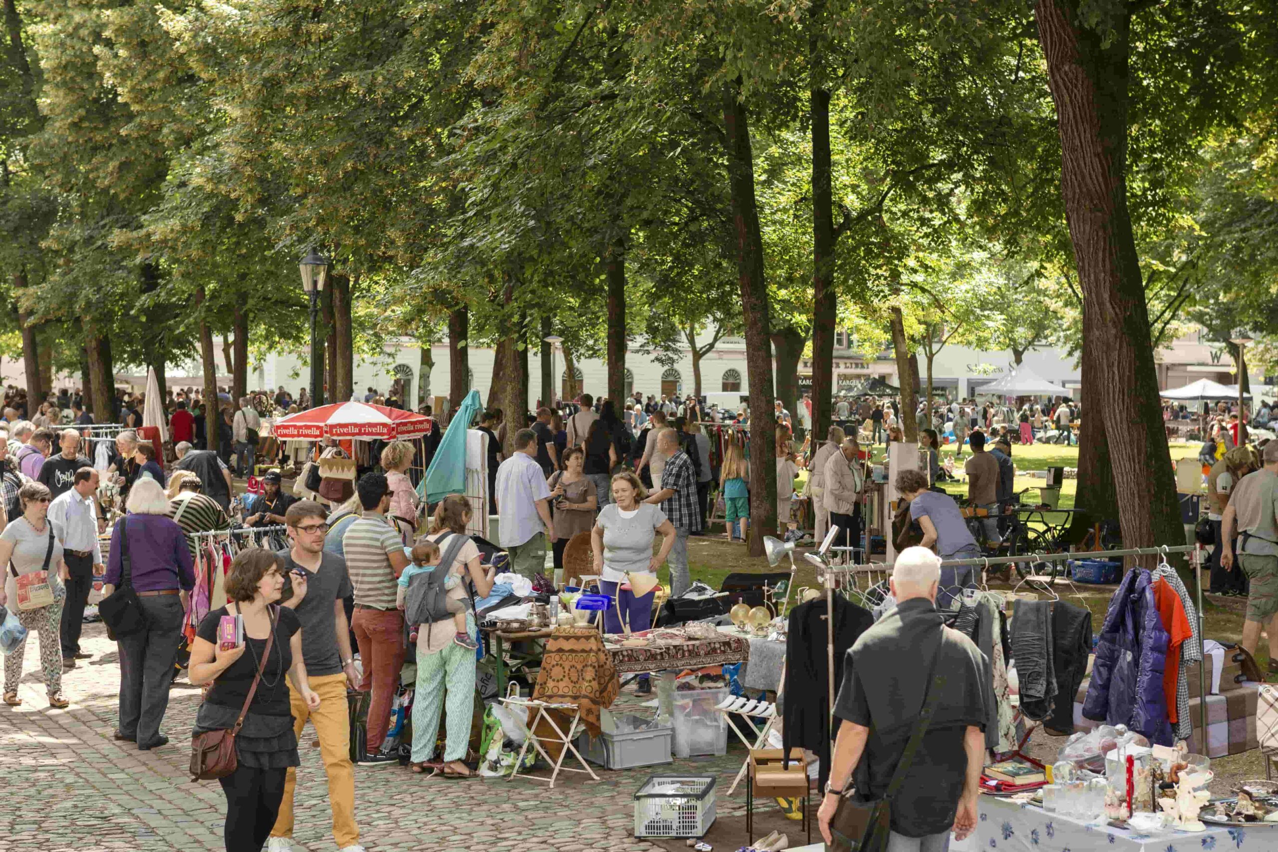 Menschen und Verkaufsstände unter Bäumen auf dem Petersplatz