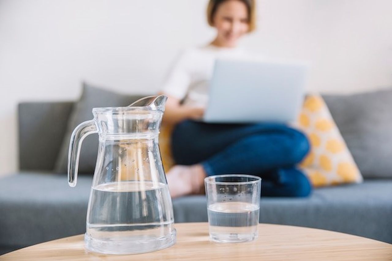 Ein Wasserkrug neben dem ein halbvolles Glas Wasser steht.